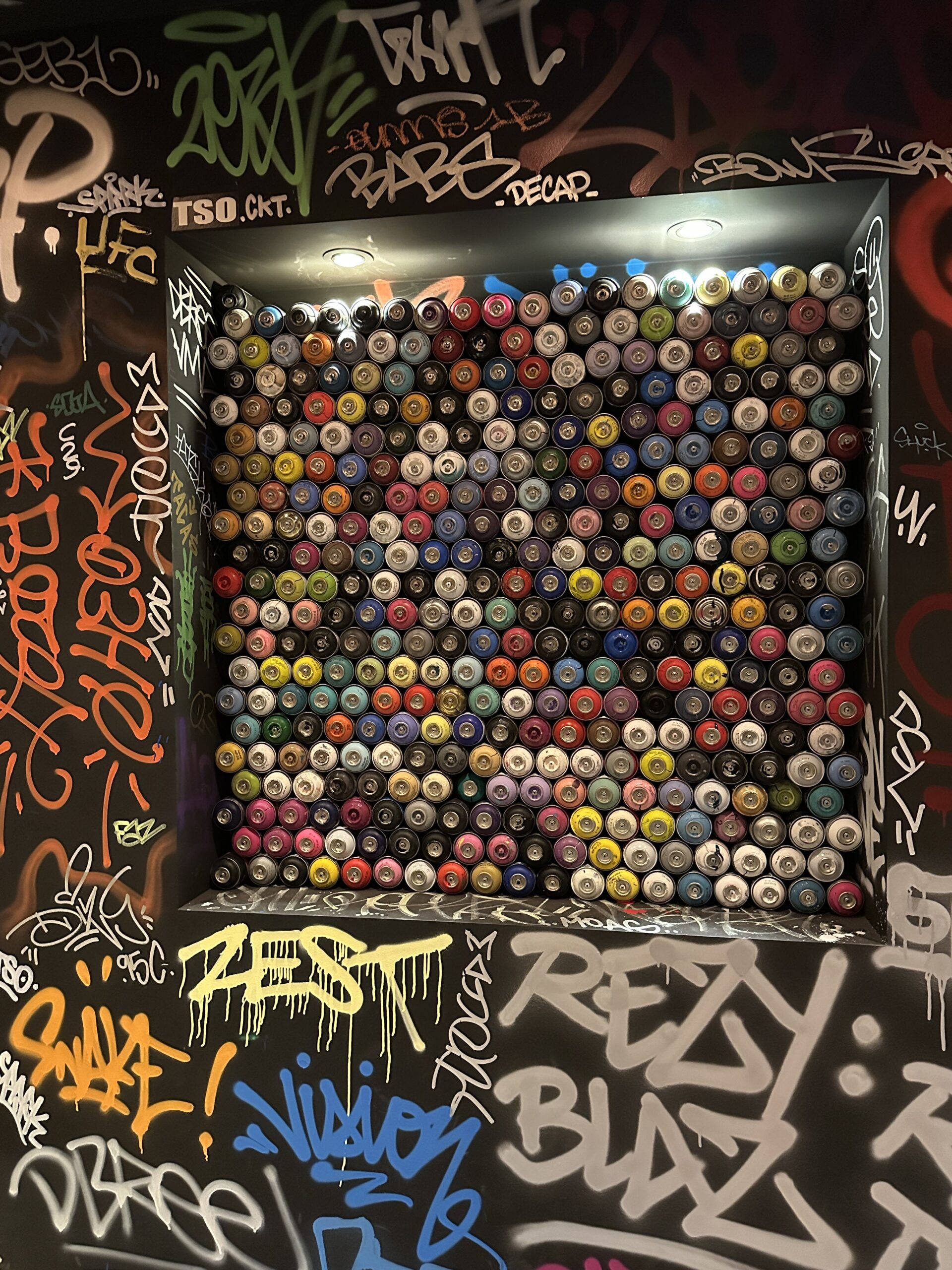 Mur orné de bombes de peinture colorées dans un décor de tags.